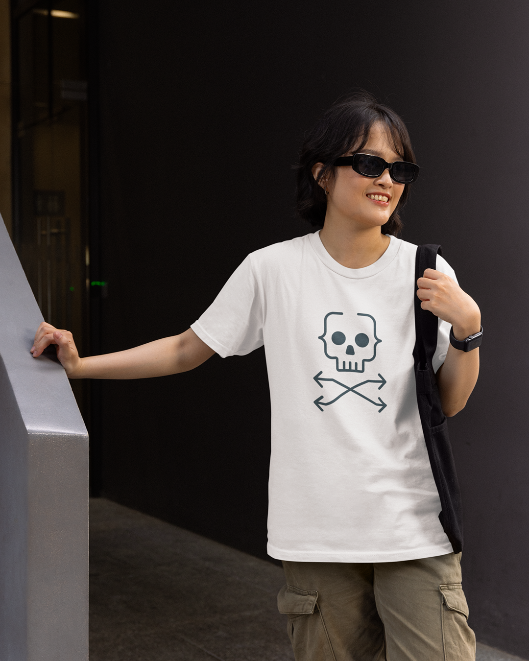 Person wearing a white t-shirt with a skull and crossbones design, standing against a dark background.