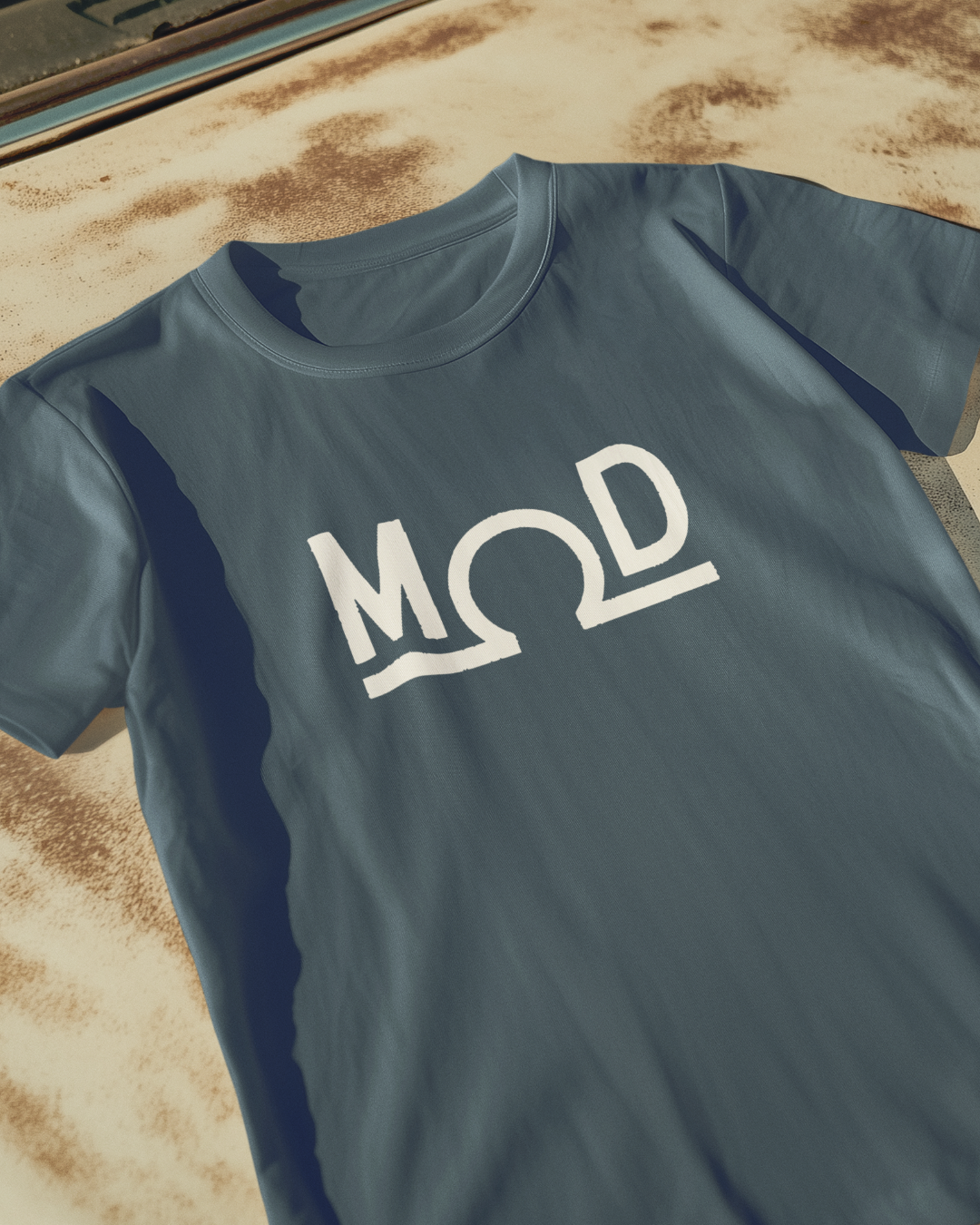 Charcoal t-shirt featuring a bold white “MOD” wordmark with the Ω (ohm) symbol as the “O” and a solid baseline
