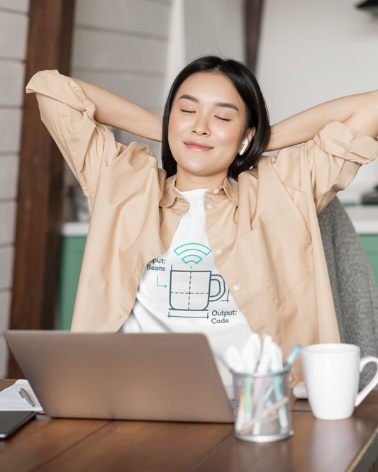 Woman relaxing with arms behind head at a desk with a laptop and coffee cup.