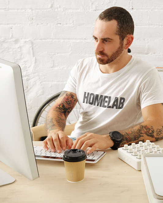 Man wearing a 'HOMELAB' t-shirt using a computer at a desk with a coffee cup.