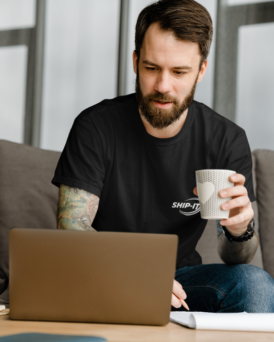 Plain balck unisex t-shirt with a small white “SHIP-IT” logo and orbit-style swoosh printed on the left chest; minimal, modern developer aesthetic on a clean studio background.