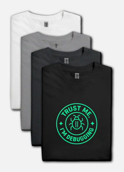 Four folded t-shirts in white, gray, and black with a green 'Trust Me, I'm Debugging' graphic on a white background.