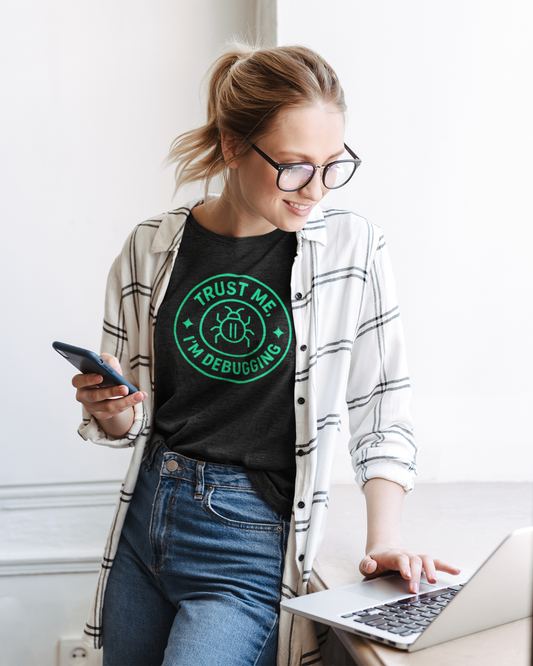 Woman wearing a black t-shirt with 'Trust Me, I'm Debugging' design, using a laptop.